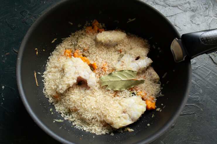 Adding the rice Raw rice spread evenly over the fish and vegetables with bay leaves