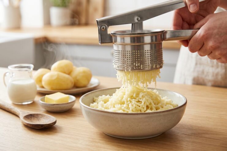 Manual potato ricer mashing potatoes Handheld potato ricer pressing boiled potatoes to create a smooth and fluffy puree.