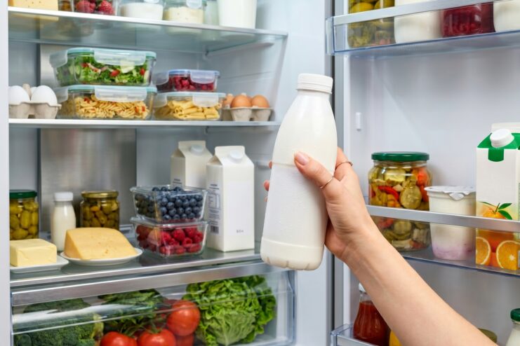 Hand grabbing a white bottle of kefir from a well-stocked refrigerator.