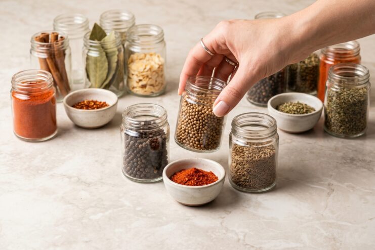 Choosing the Right Spices A hand selects a jar of coriander seeds among other spices on a table.