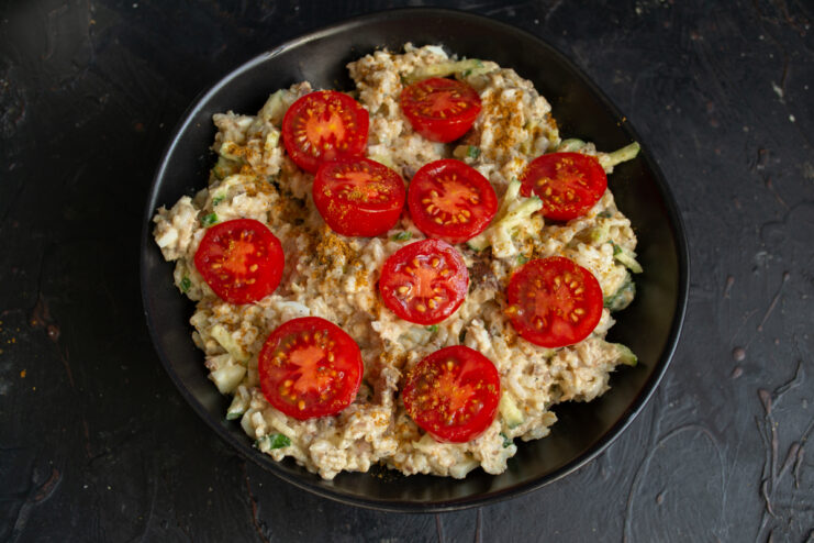 Final plating Fish salad served on a black plate decorated with cherry tomato halves