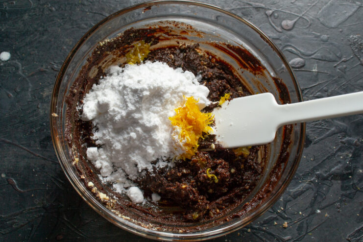 Adding zest and powdered sugar Sifting powdered sugar and grating fresh lemon zest over the chocolate mixture