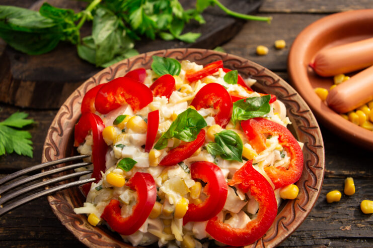 Sausage salad with corn and red bell pepper on a serving plate.