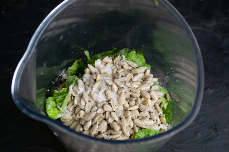 Adding Seeds and Seasonings Sunflower seeds and salt on top of fresh greens inside a blender cup