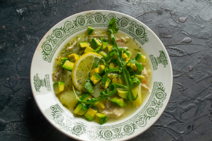 Serving the soup with avocado Ladling hot chicken soup over diced avocado and greens in a deep bowl