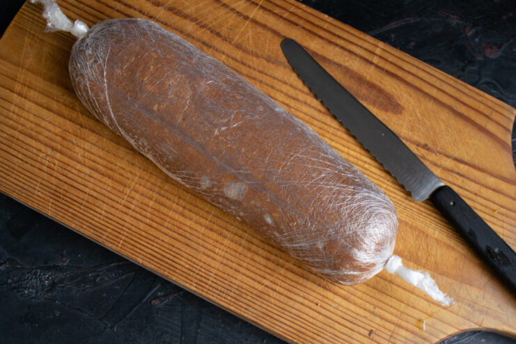 Salami ready for chilling Formed chocolate salami wrapped tightly in plastic wrap on a wooden board