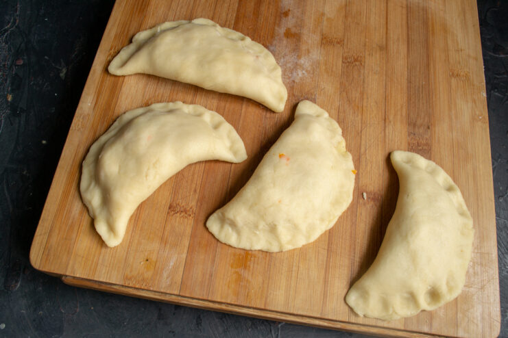 Sealing the hand pies before frying Formed half-moon shaped hand pies resting on a wooden board