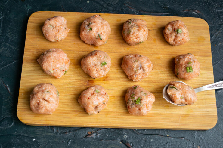 Shaping the fish meatballs Perfectly shaped raw fish meatballs arranged on a wooden cutting board