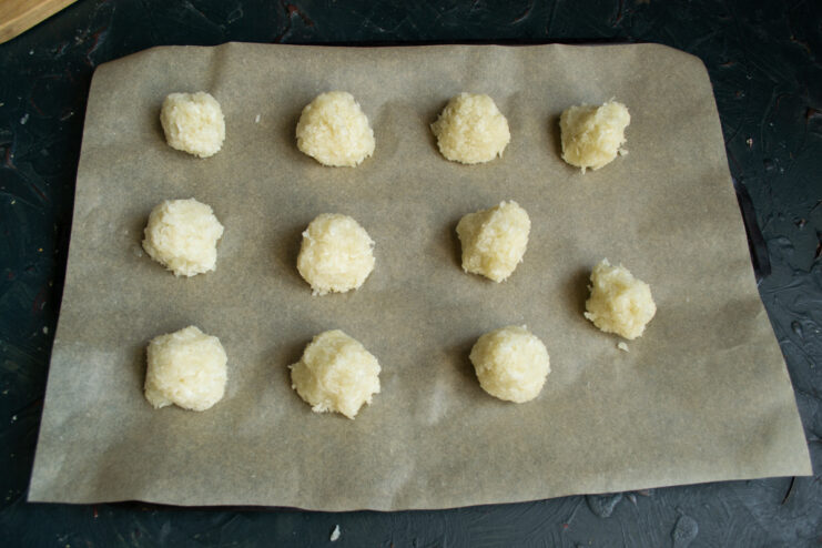 Shaping the raw coconut cookies. Perfectly round raw coconut dough balls arranged on a parchment-lined baking sheet.