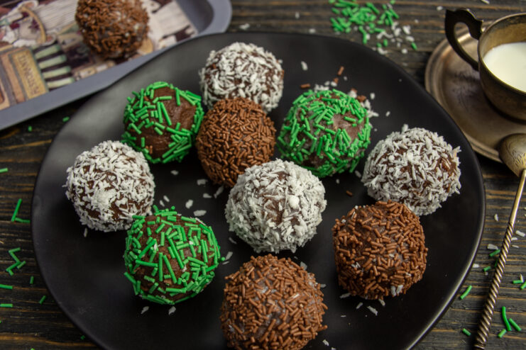 Chocolate and mascarpone petits fours with colorful sprinkles on a black plate.