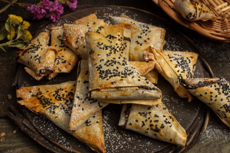 Baked sweet samosas with raisins and poppy seeds dusted with powdered sugar and black sesame