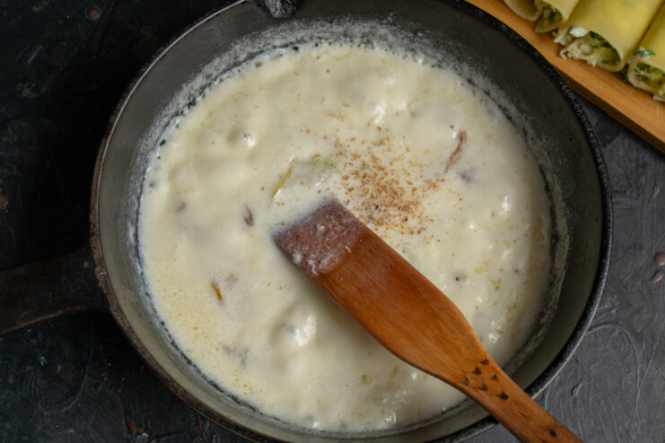 Whisking the cream sauce Creamy béchamel sauce simmering with nutmeg in a pan