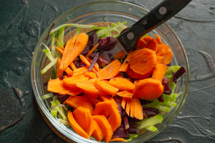 Adding Orange Carrots Layer of sliced orange carrots on top of other vegetables in a bowl