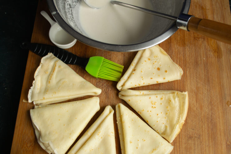 Cooked crepes folded into triangles resting on a board