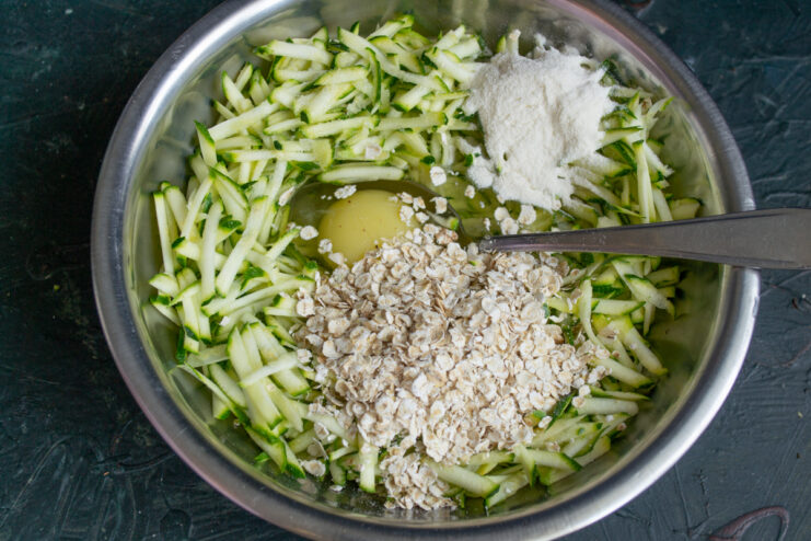 Mixing the batter Mixing grated zucchini with an egg, flour, and oats in a bowl.