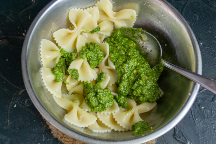 Mixing pasta with sauce Mixing cooked farfalle pasta with fresh green pesto in a bowl