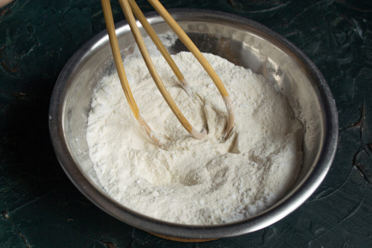 Mixing dry ingredients for the dough Whisking wheat flour and fine white sugar in a metal mixing bowl
