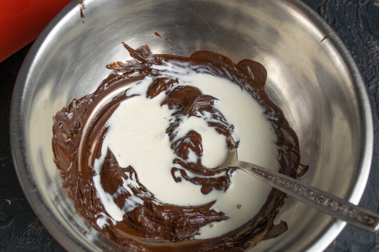 Mixing melted chocolate with hot heavy cream in a bowl.