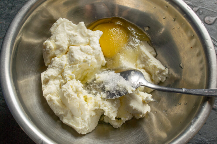 Mixing farmers cheese with an egg and sugar in a bowl
