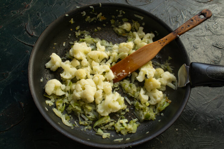 Combining The Vegetables Mixing boiled cauliflower and sautéed onions together in a skillet