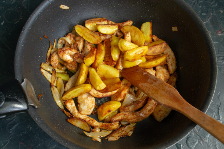 Combining the ojakhuri ingredients Mixing fried potatoes and chicken together in a skillet