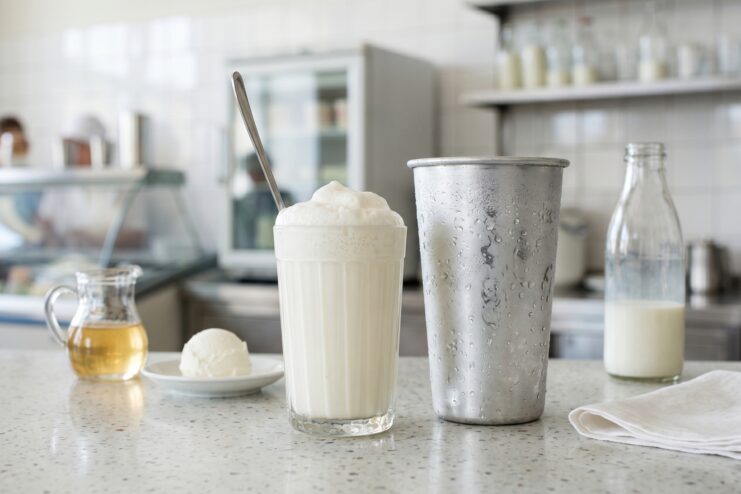 Classic Grocery Store Milkshake A classic Soviet-style milkshake in a tall glass next to a metal blending cup and syrup.