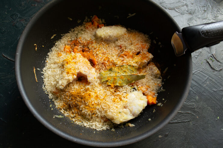 Spices for the fish plov Sprinkling paprika and cumin over raw rice in a skillet