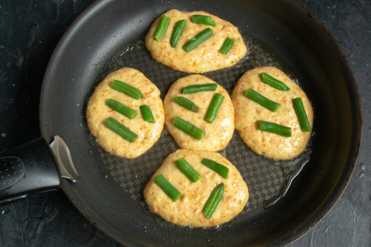Adding The Bean Topping Green beans placed on top of potato fritter batter in a skillet