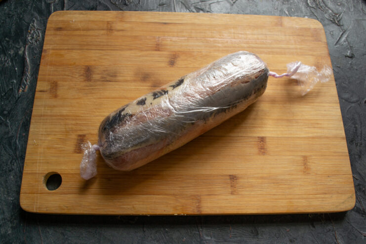 Rolled herring tightly wrapped in clear plastic wrap.
