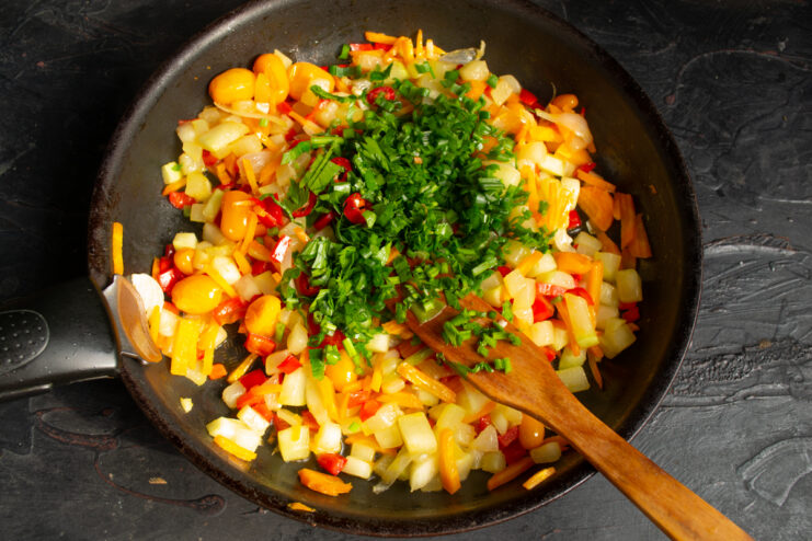 Freshly chopped herbs added to the cooked vegetables in the skillet.