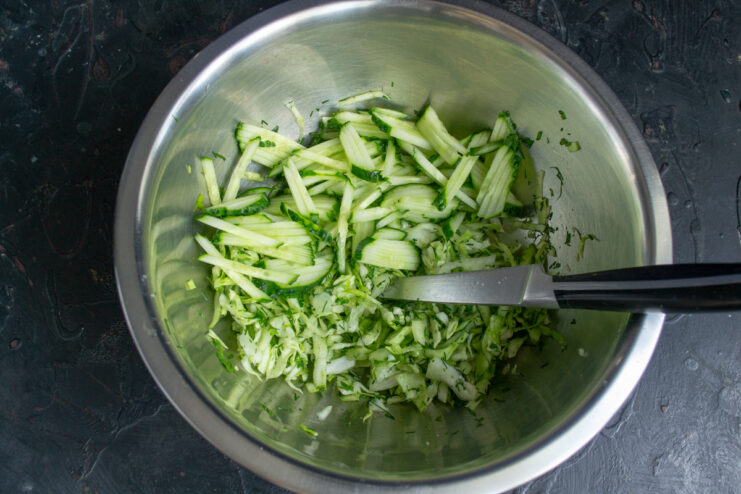 Adding Cucumbers to the Salad Fresh cucumbers cut into thin julienne strips added on top of shredded cabbage.