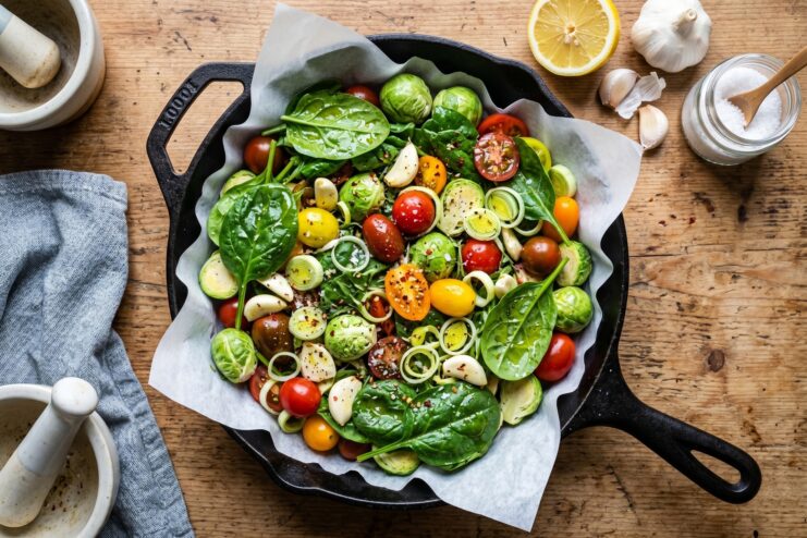 Fresh spinach, cherry tomatoes, leeks, and Brussels sprouts arranged in a skillet.