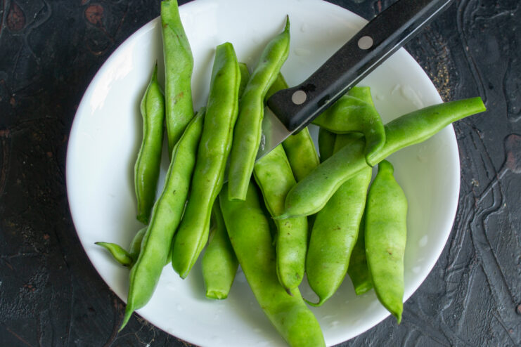 Fresh raw green beans resting on a white plate