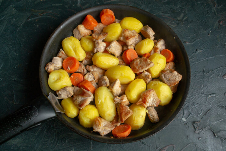 Combining Meat and Vegetables Seared pork, parboiled potatoes, and carrots mixed in a skillet.