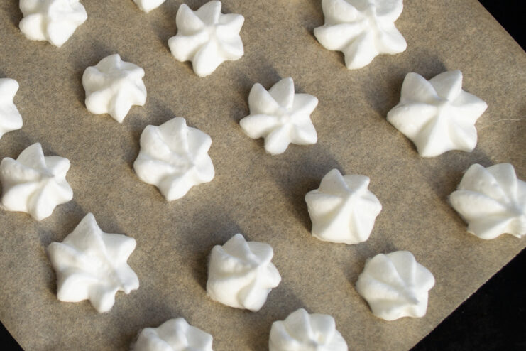 Piping the meringue Piping raw meringue onto parchment paper on a baking sheet