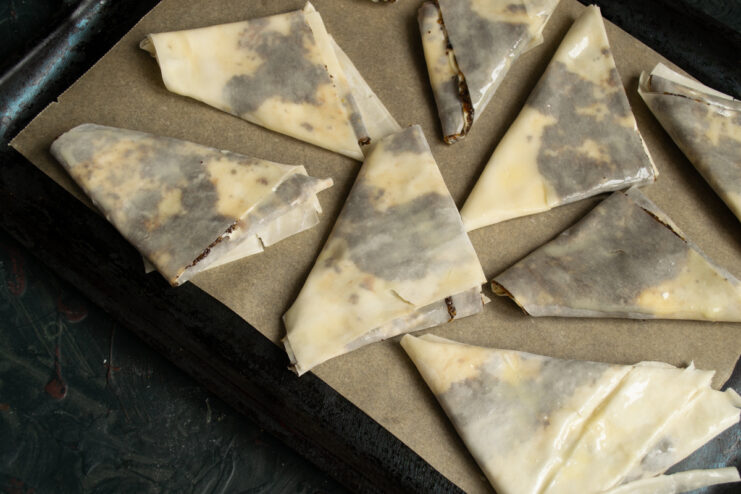 Preparing for Baking Raw folded samosas arranged on a parchment-lined baking sheet