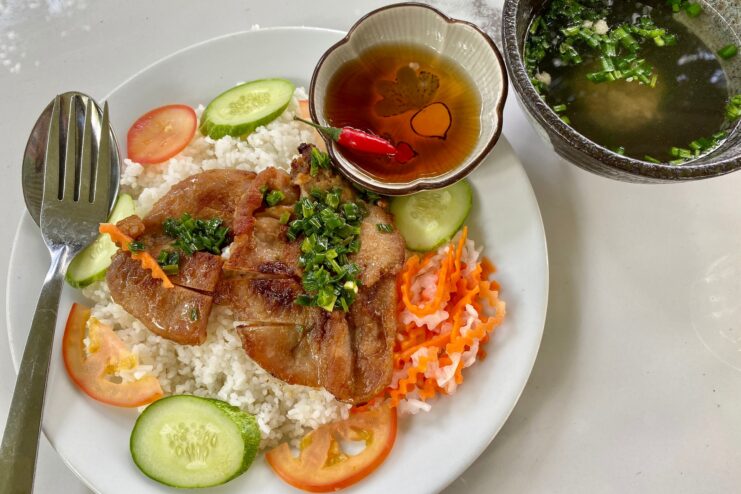 Com tam broken rice plate with grilled pork chop Plate of com tam broken rice served with a grilled pork chop and pickled vegetables.