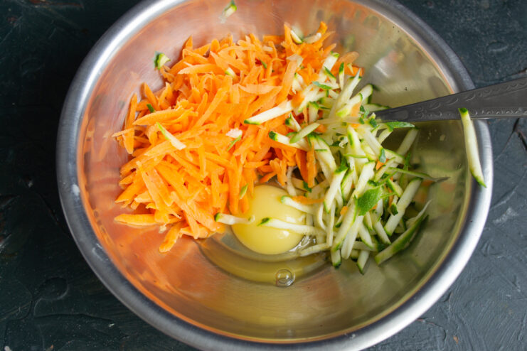 Preparing the vegetable fritter base Grated carrots, zucchini, and an egg in a mixing bowl