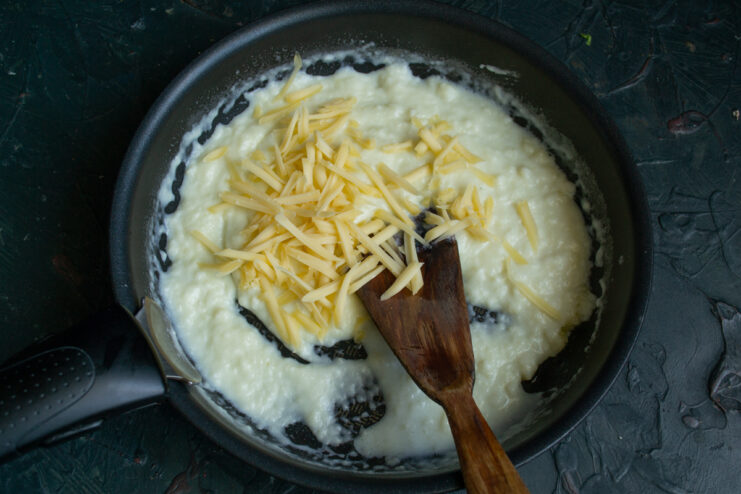 Melting cheese into the sauce Grated hard cheese melting into a creamy sauce in a skillet