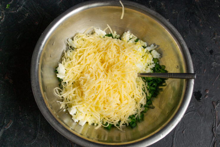 Adding grated suluguni cheese Grated suluguni cheese added to the egg and scallion mixture