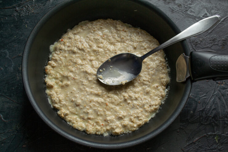 Frying The Oat Pancake Thick oat batter being spread evenly onto a hot greased skillet with a spoon