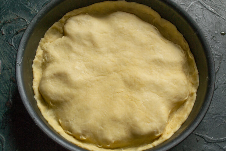 Forming the Base Raw pastry dough snugly tucked over pears in a round skillet