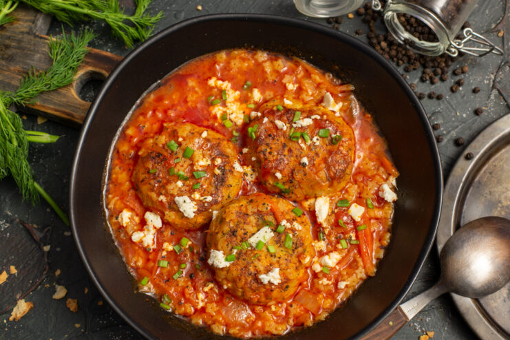 Bowl of tomato soup with large chicken meatballs, sprinkled with crumbled feta and green onions.