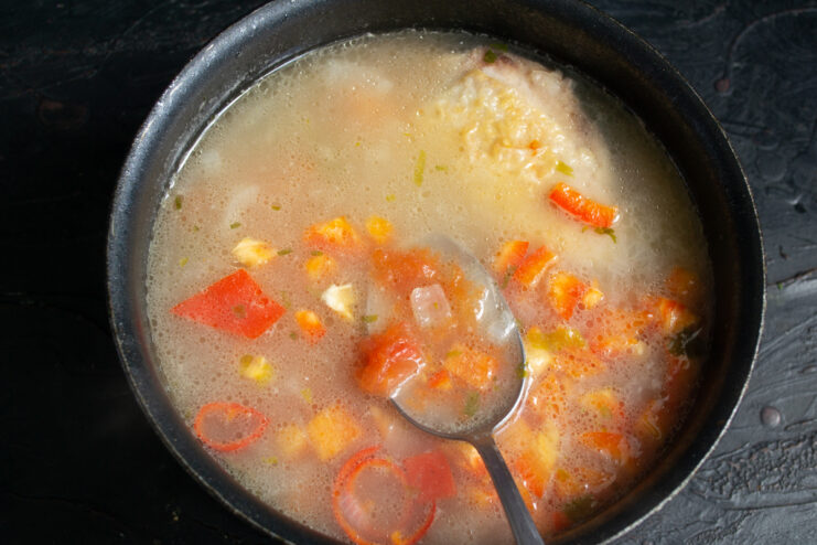Adding Tomatoes And Peppers Stirring chopped tomatoes and red peppers into the simmering soup