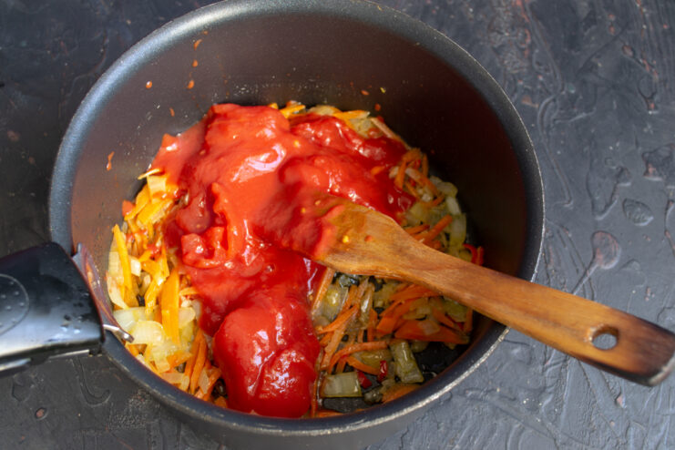 Adding The Tomatoes Canned tomatoes poured into a pot with sautéed vegetables.