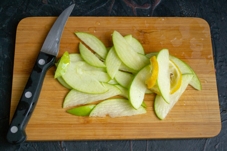 Thin slices of green apple with a lemon on a cutting board