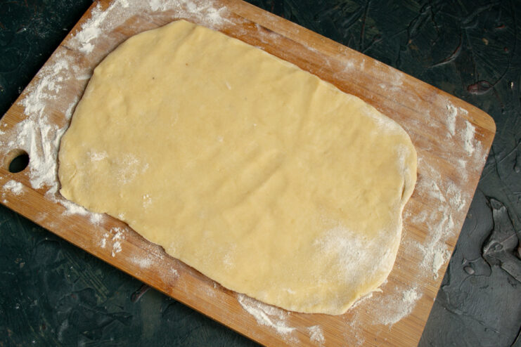 Rolling the Dough Flat Thinly rolled rectangular sheet of dough on a wooden cutting board