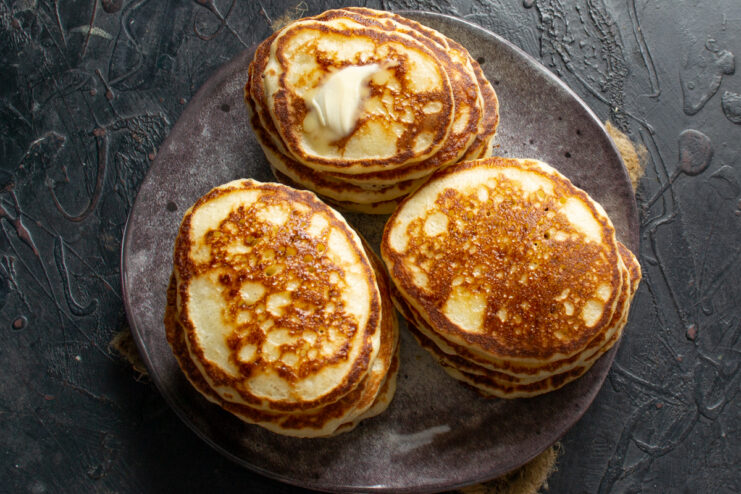 Three stacks of fluffy pancakes with butter on a serving platter