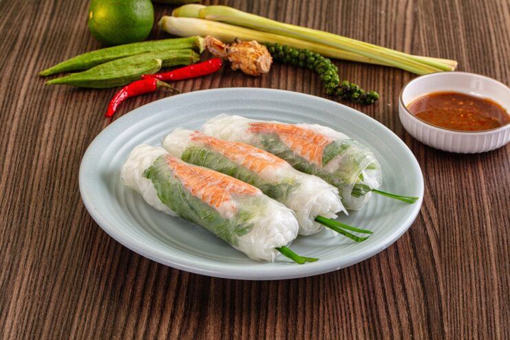 Fresh goi cuon spring rolls with shrimp Three fresh goi cuon spring rolls filled with shrimp and herbs on a plate.