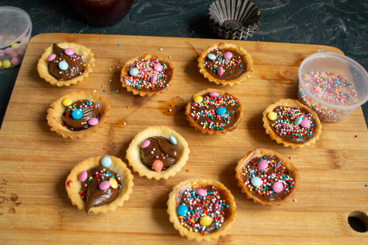 Decorating the tartlets with vibrant sprinkles Decorating the chocolate tartlets with colorful dragées and sprinkles